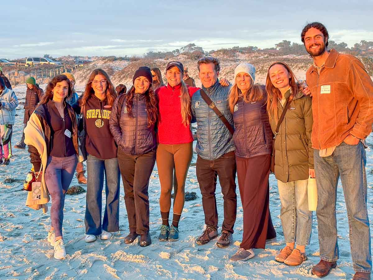 Eight Surfrider conference participants gather for group shot, standing on the beach in the sunset light. Photo: Harry Parker