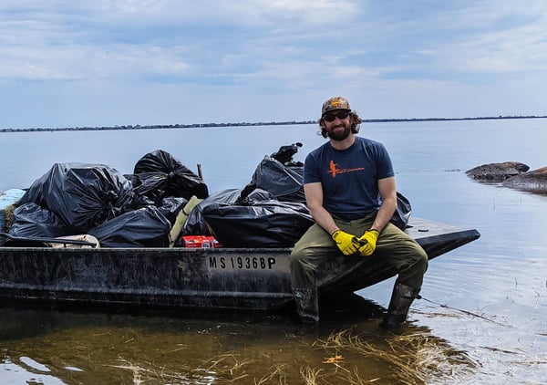 Chris Borgatti With The Massachusetts Chapter sitting on a boat that has trash bags full of trash collected from a beach cleanup