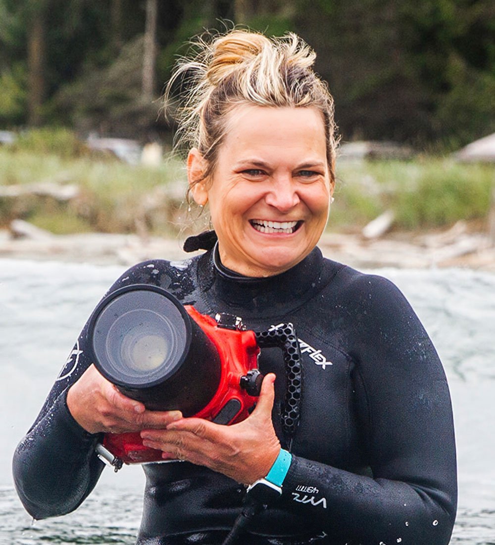 Kelly Jones With the Surfrider South Sound Chapter holding her camera while wearing a wetsuit.