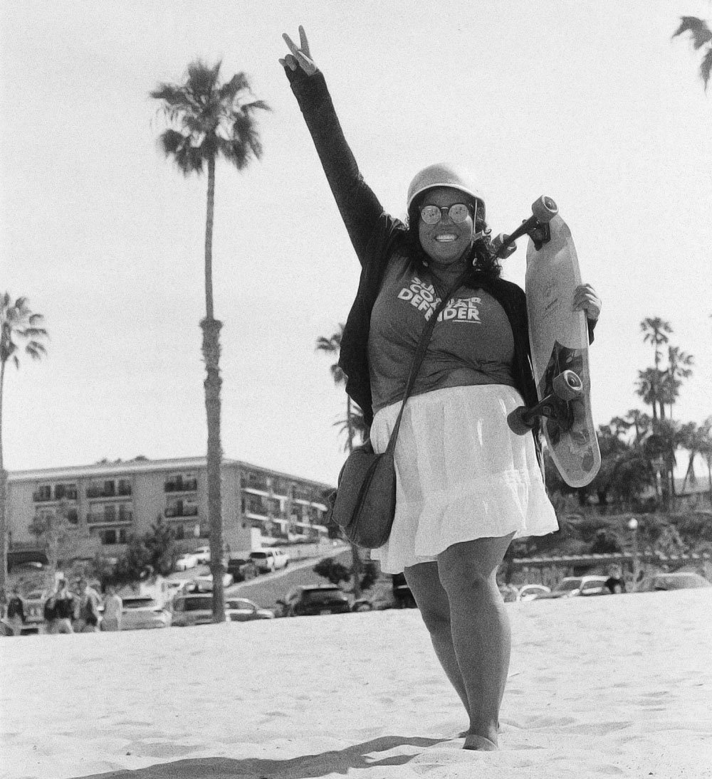 Andrika Payne with the Los Angeles chapter walking on the beach holding a skateboard