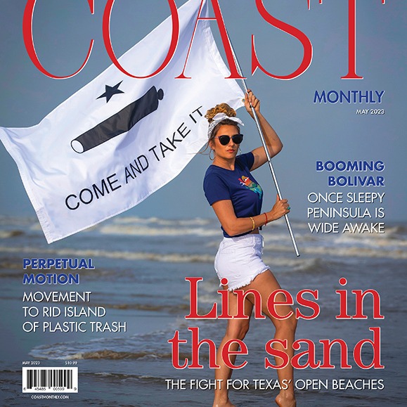 Coast Monthly May 2023 Cover Shot with woman standing on beach holding flag with Come and Take Me slogan