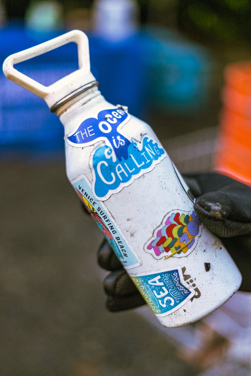 Close up view of a dirty water bottle found during a beach cleanup with "save the ocean" stickers on it