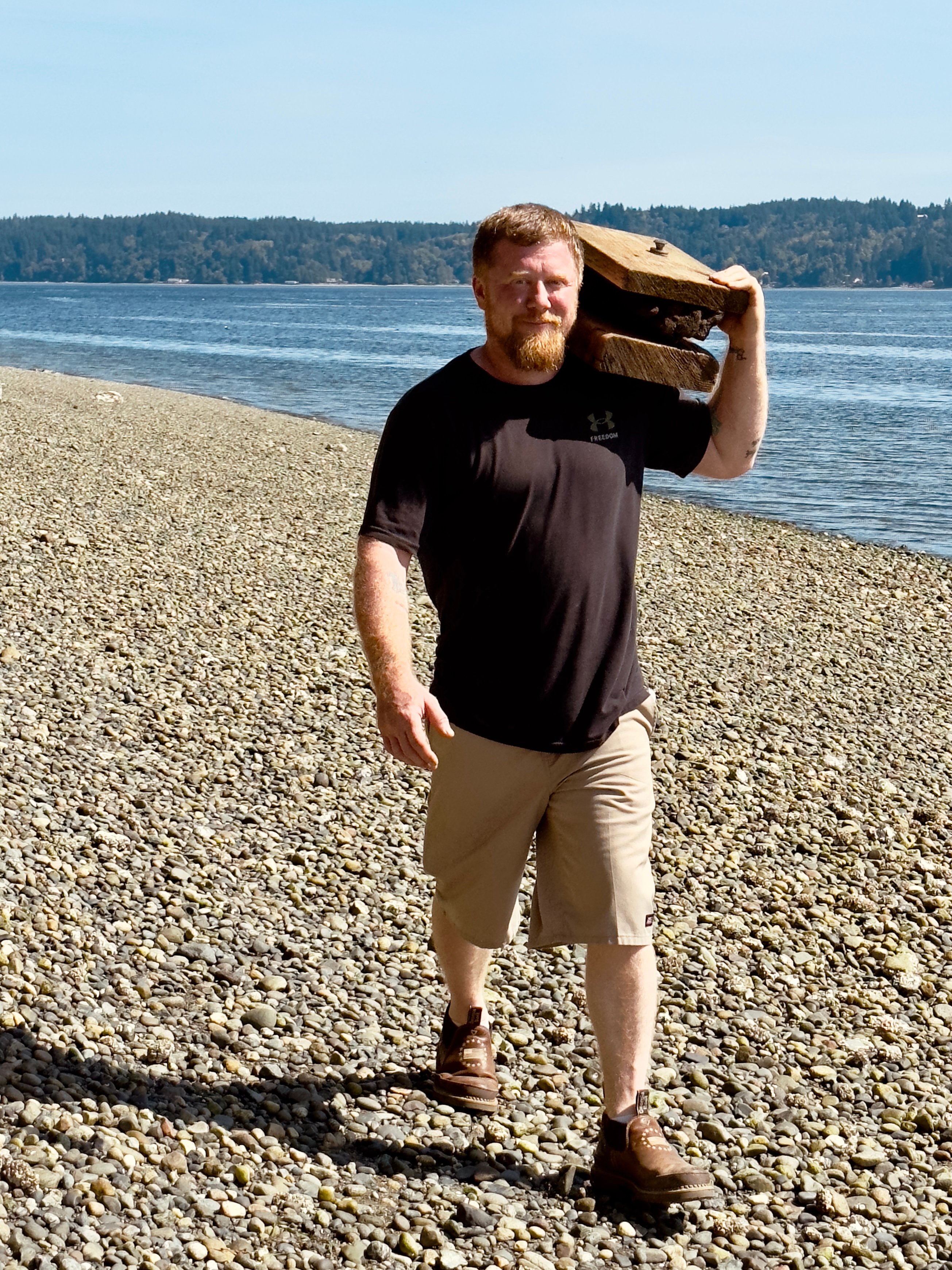 Male volunteer carrying a large heavy piece of cement debris on his shoulder during a beach cleanup