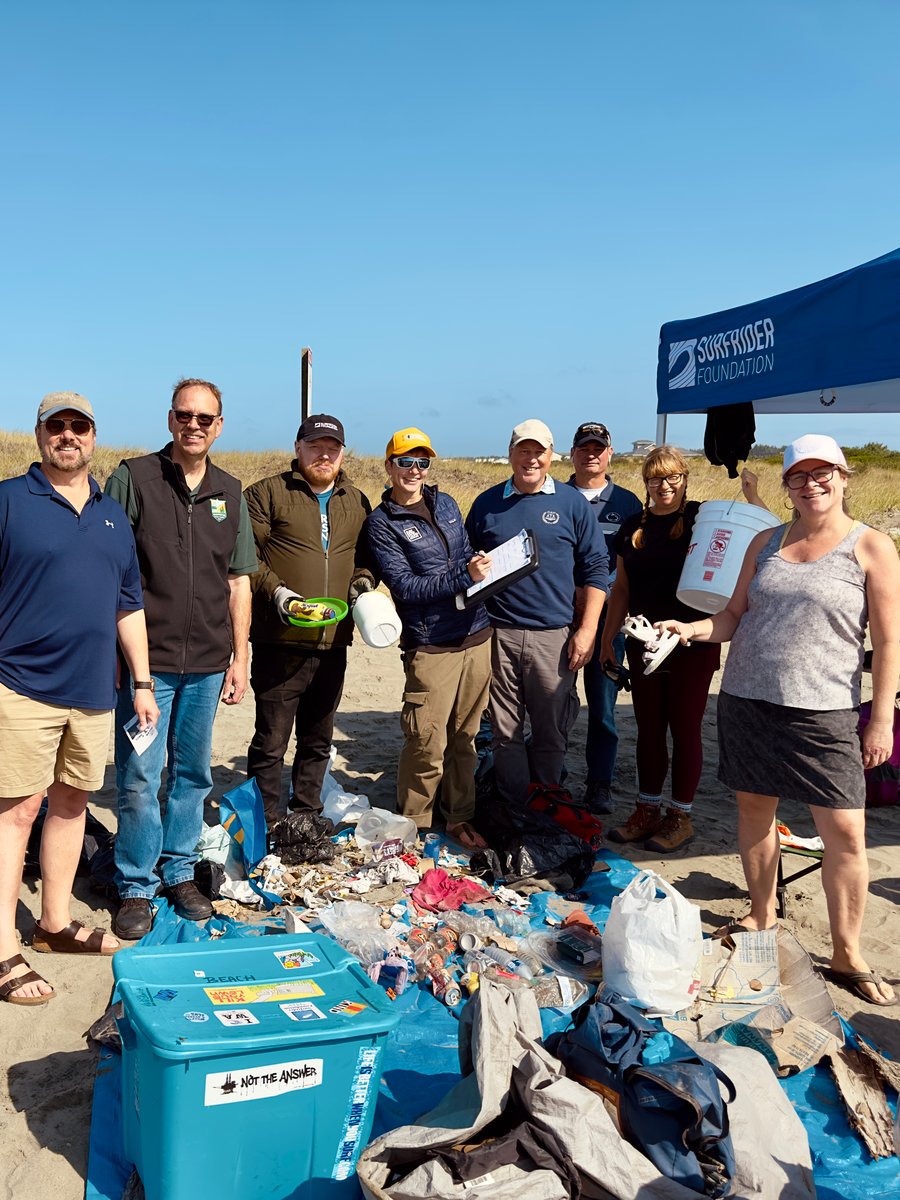 Group of volunteers standing proudly behind all the trash they collected and reported at a beach cleanup