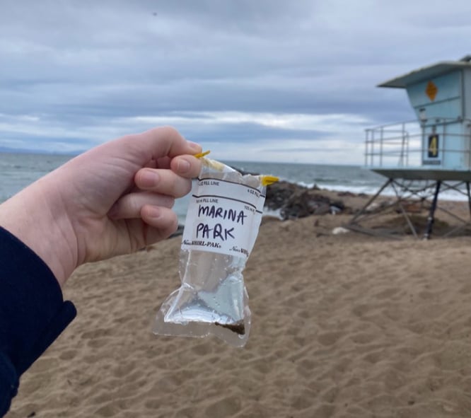 Water sample in a plastic baggie from Marina Park with a lifeguard tower in the background. 