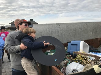 Parents lift their children to add their collected litter to the dumpster.