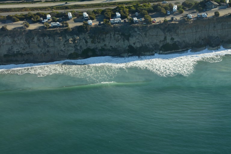 Aerial photograph of several threatened campsites at South Carlsbad State Beach during the 2021 King Tides. The campground is situated at the edge of a coastal bluff; the high tide has overtaken the beach and is chipping away at the bluff's bottom.