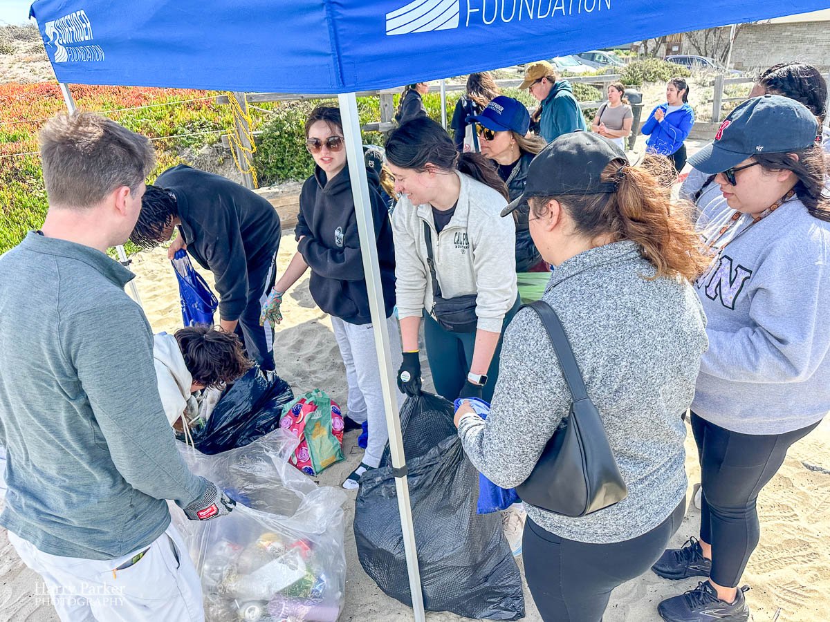 Crowd of Volunteers work together under Surfrider tent sorting garbage