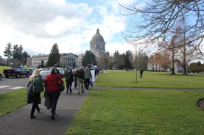 Volunteers walk along the sidewalk leading up to the Olympia Capitol building on a sunny day 
