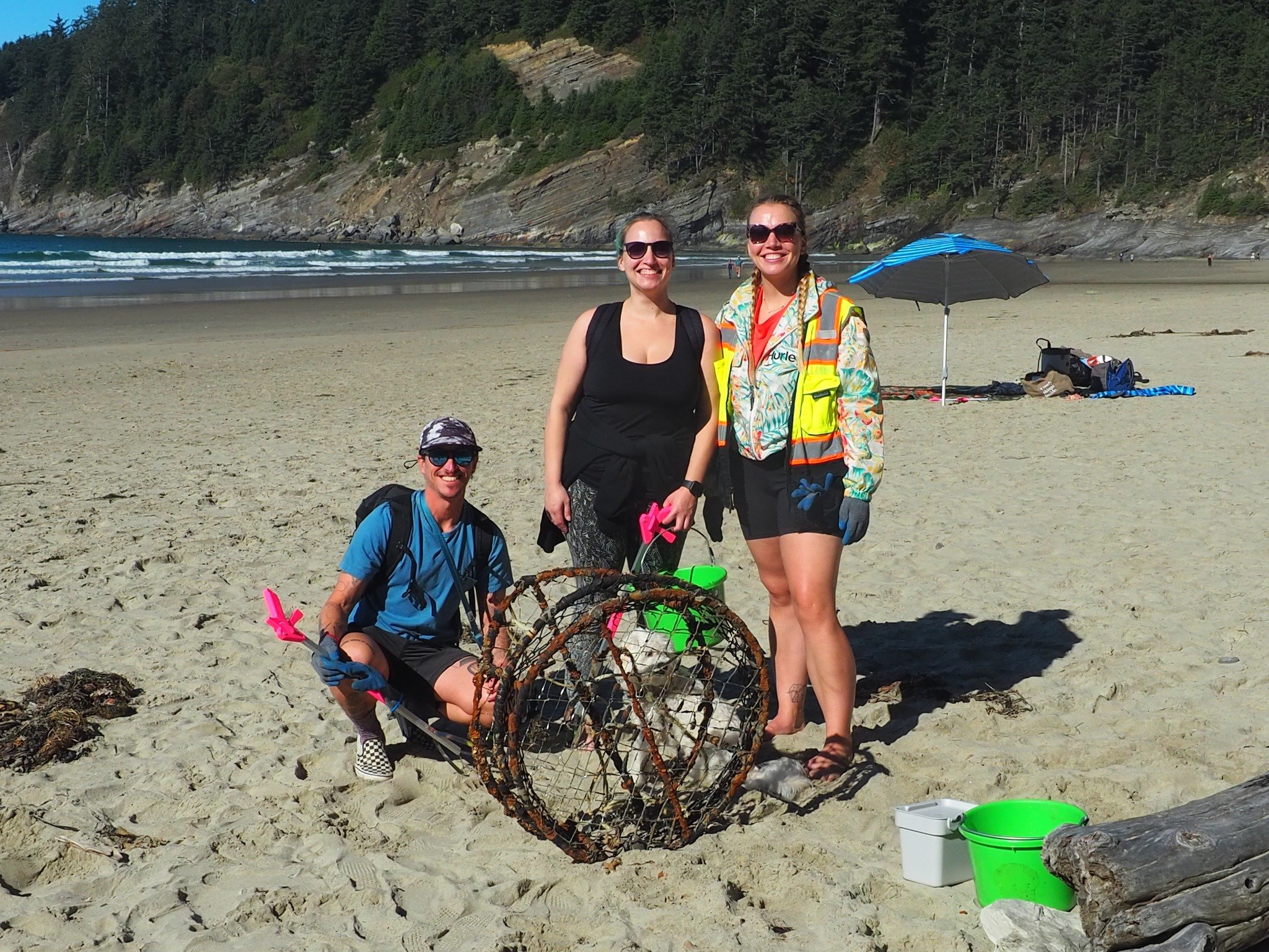 three volunteers pose with a derelict crab pot they collected during a beach cleanup at Short Sands Beach