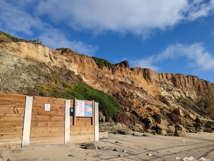 A wooden seawall on the beach in Del Mar separates the beach from the bluffs. Recent bluff slide activity is apparent next to where the seawall ends.