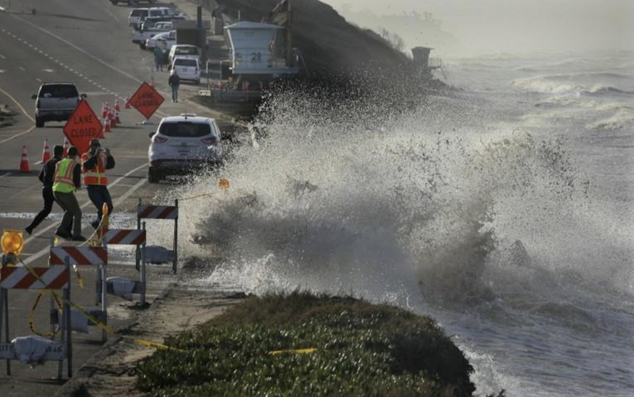 Construction crews retreat as a large wave laps onto the street during El Niño swells of 2015/16. The road is partially closed in the flood zone.