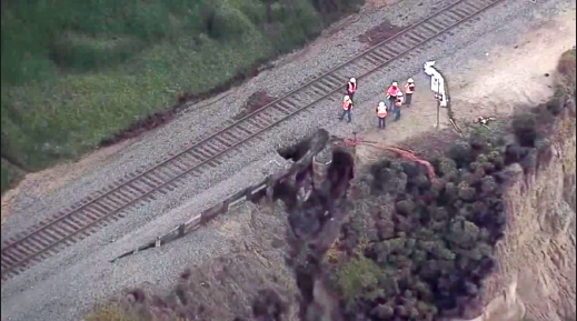 Overhead view of workers hovering near the train tracks, where a sinkhole in the bluff has emerged only 6-7 feet from the tracks.