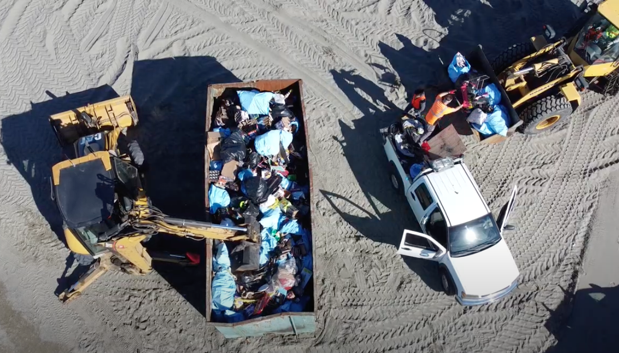 Aerial view of a backhoe and frontloader filling a large dumpster with cleanup debris