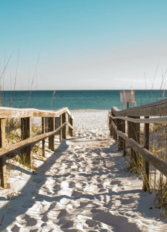 A sandy beach walkway leading down to a calm sunny day on the beach