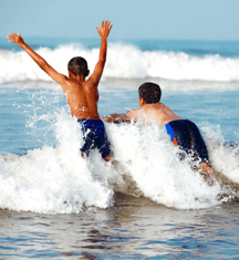 Two kids leaping into a small breaking wave 