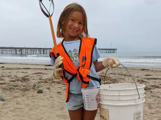 A tiny volunteer with a bucket and grabber at a cleanup