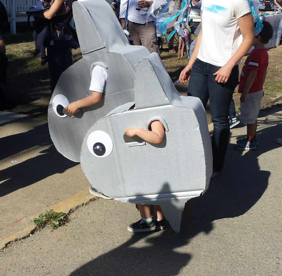 Two children wearing silver fish costumes with large eyes