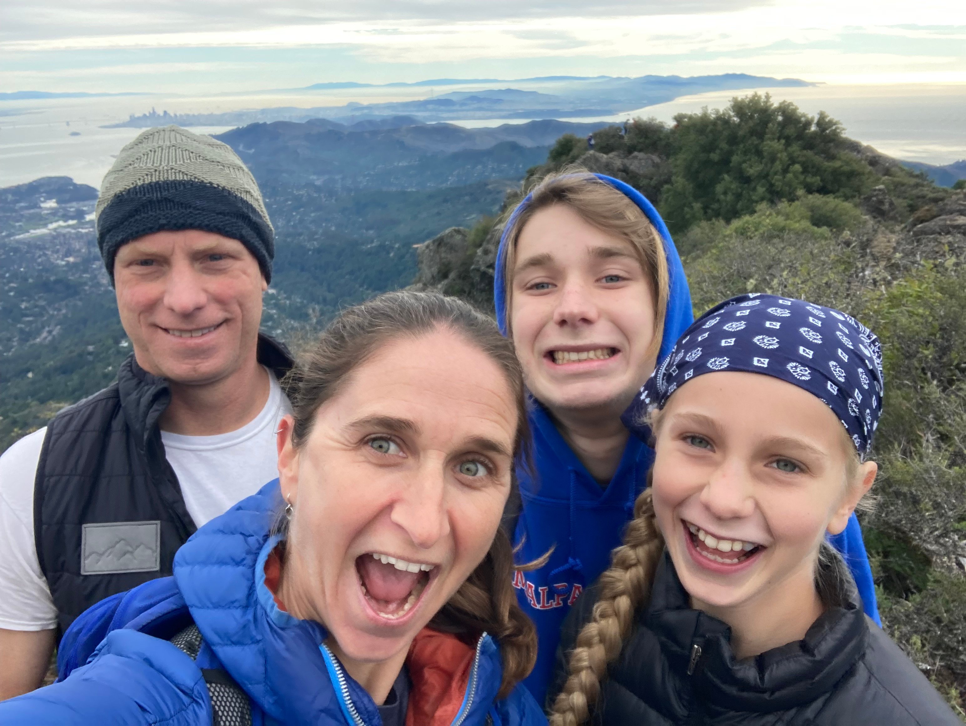 Man, woman, boy, and girl at the top of a mountain peak with the bay in the background