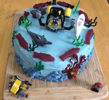 Blue cake with wave frosting, fish, remotely operated vehicles, octopus, and sharks decorating it