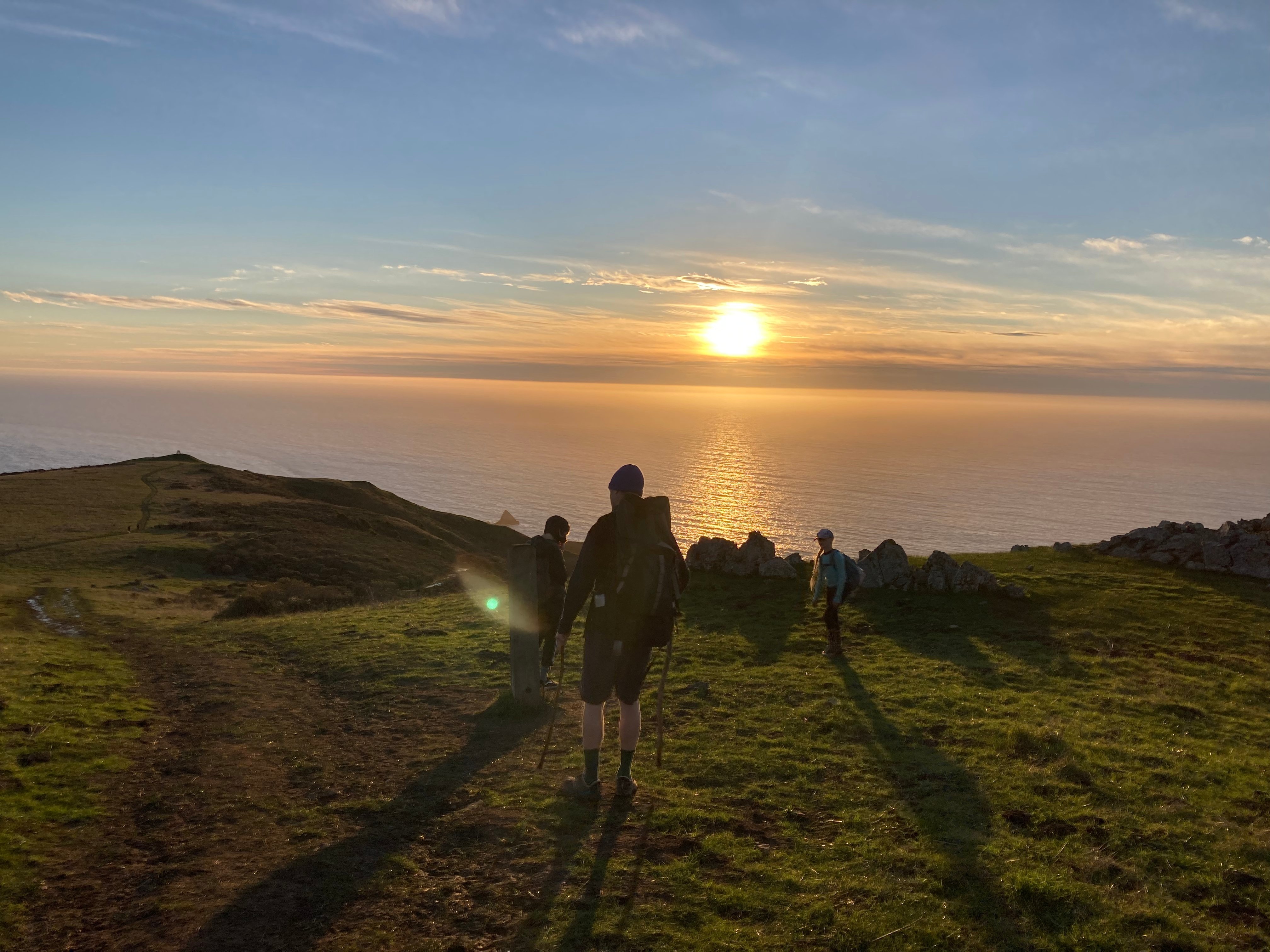 People silhouetted on a coastal trail with ocean in background at sunset