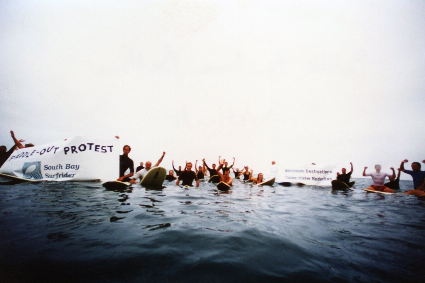 A group of surfers in the water holding protest banners