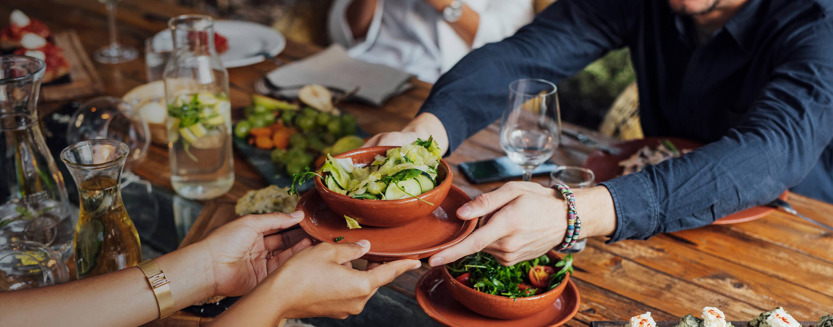 A group of people share a meal at an ocean friendly restaurant. Two people are passing a bowl of food across the table. 