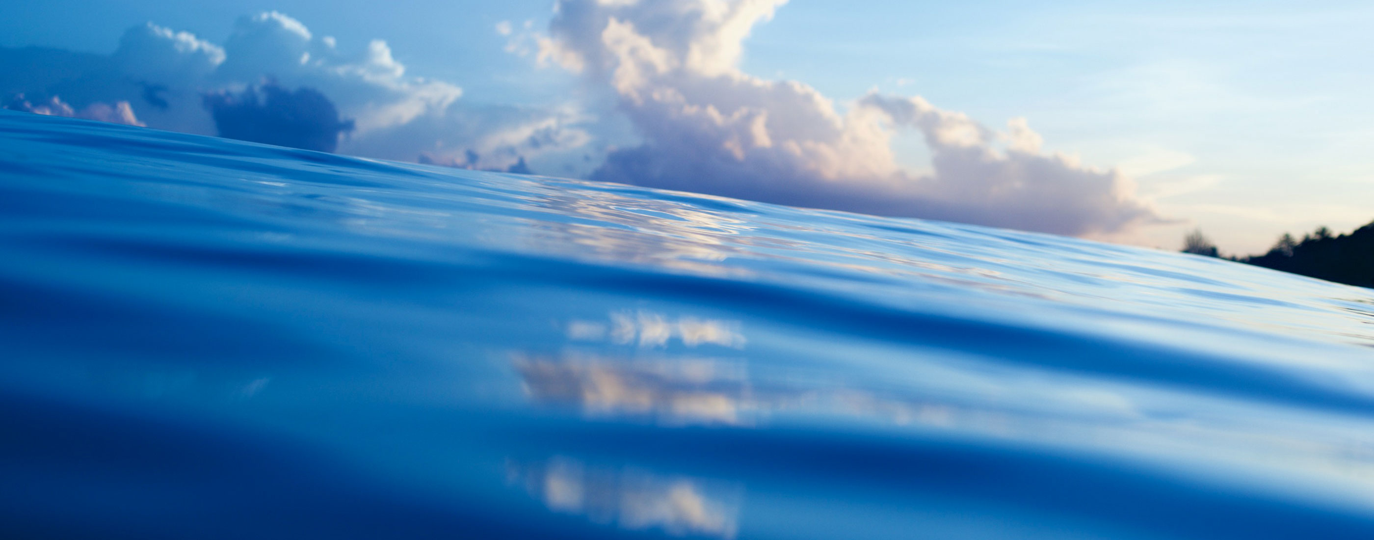 Ocean water surface in the foreground with large clouds over the horizon line in the background.