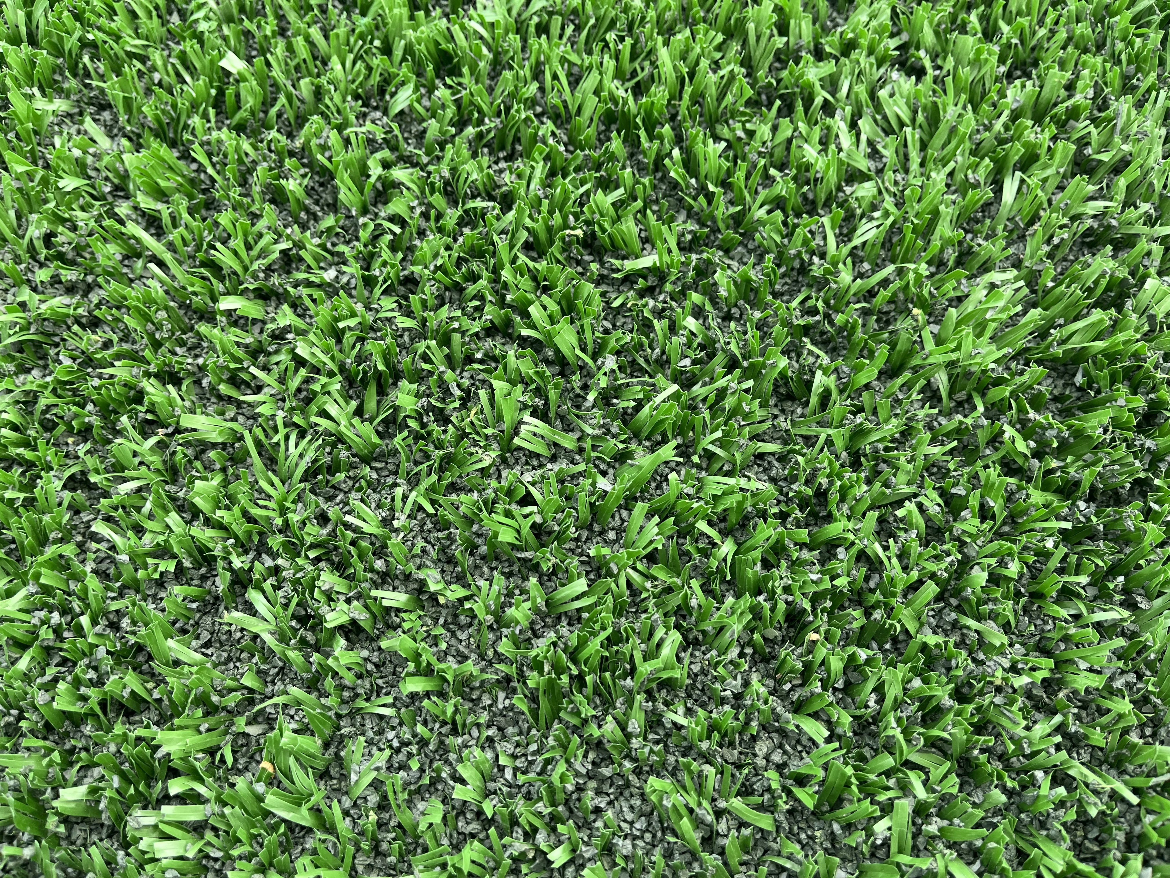 a close up of green plastic turf with rubber pellet infill