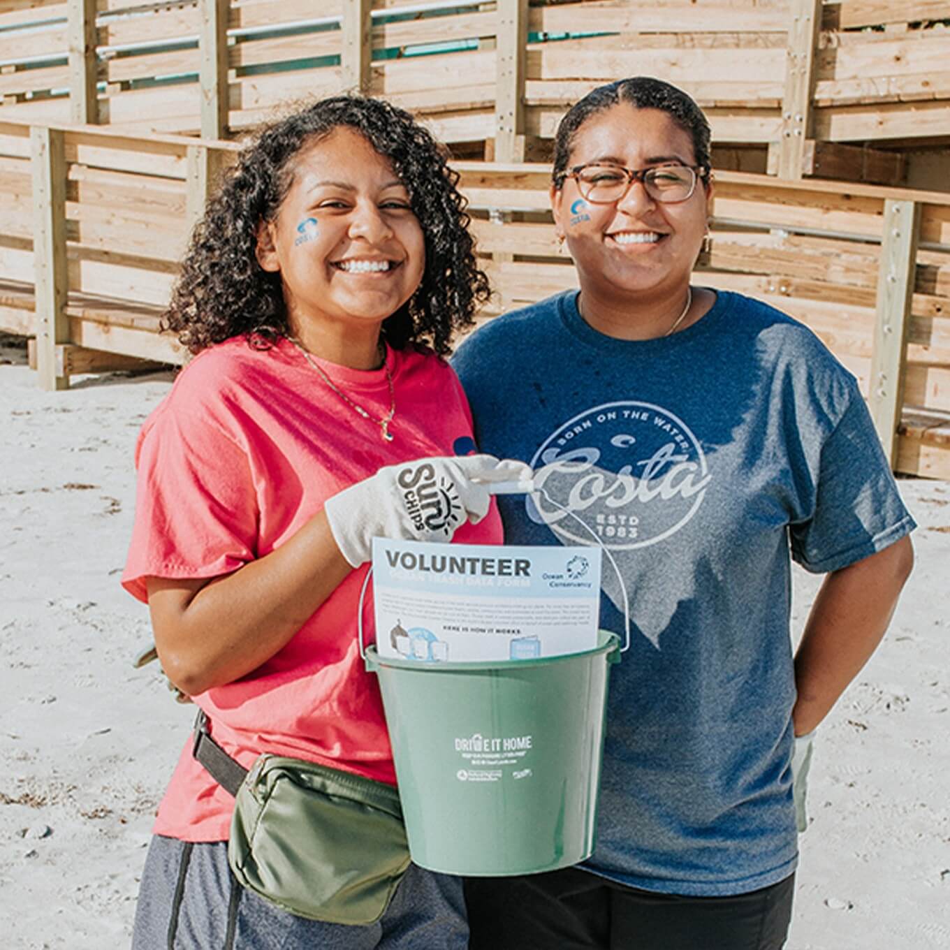 two women holding a bucket of trash collected at a beach cleanup