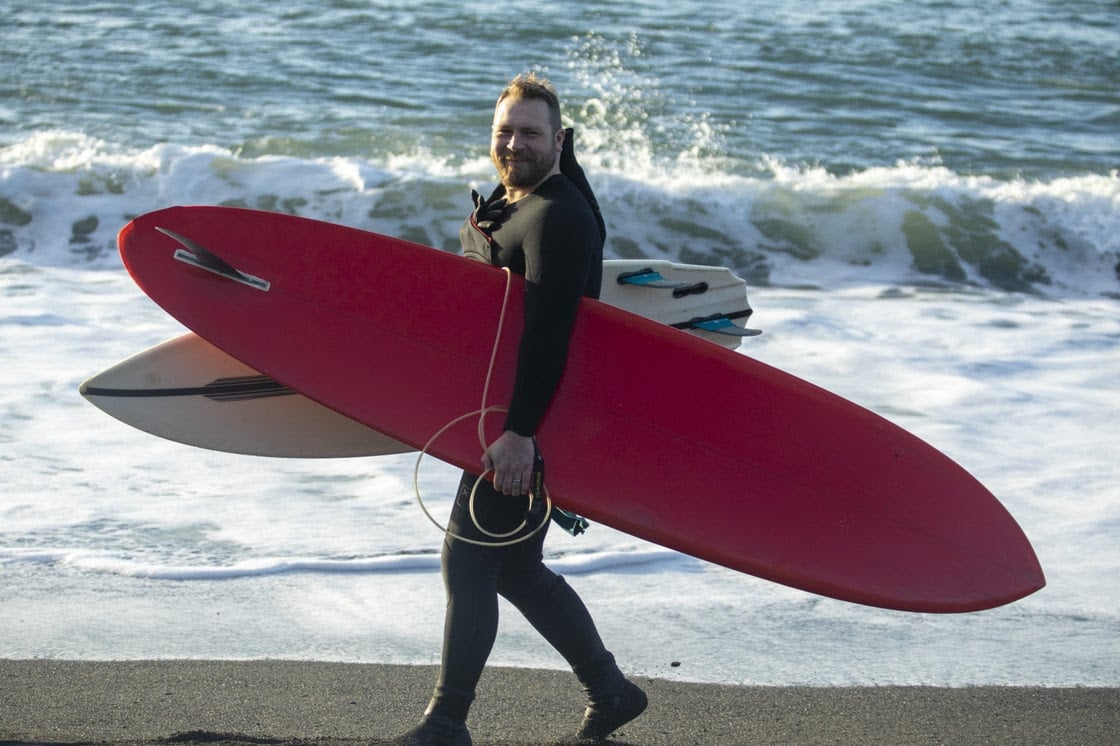 Pete double-fisting surfboards walking along the beach