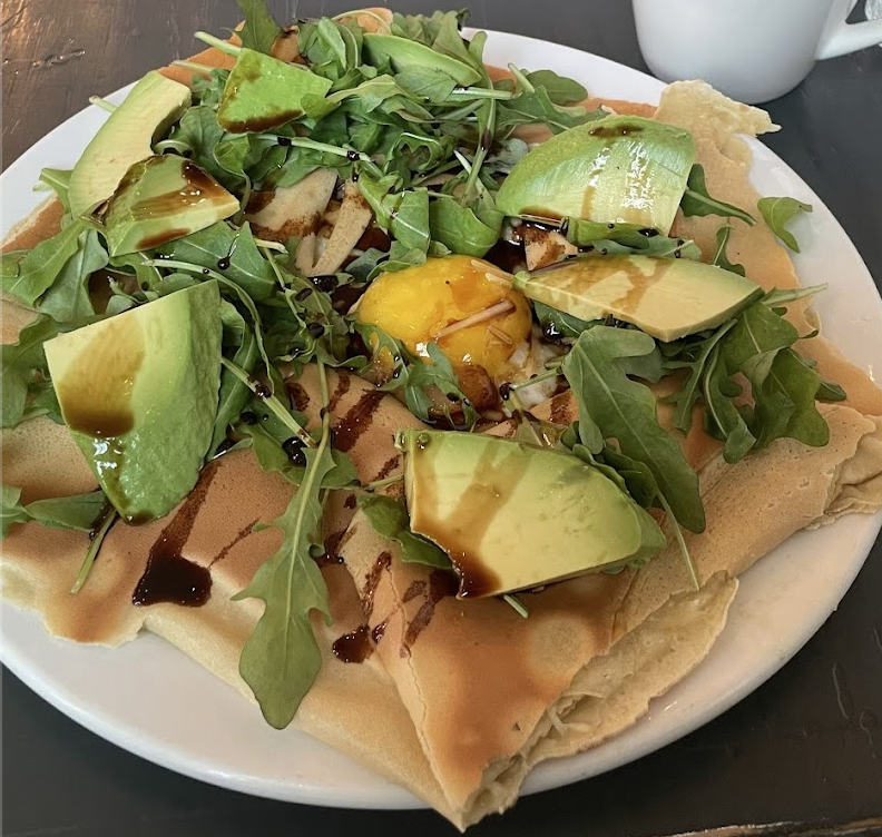 A star-shaped pastry covered in fresh arugula and avocado with an egg in the center