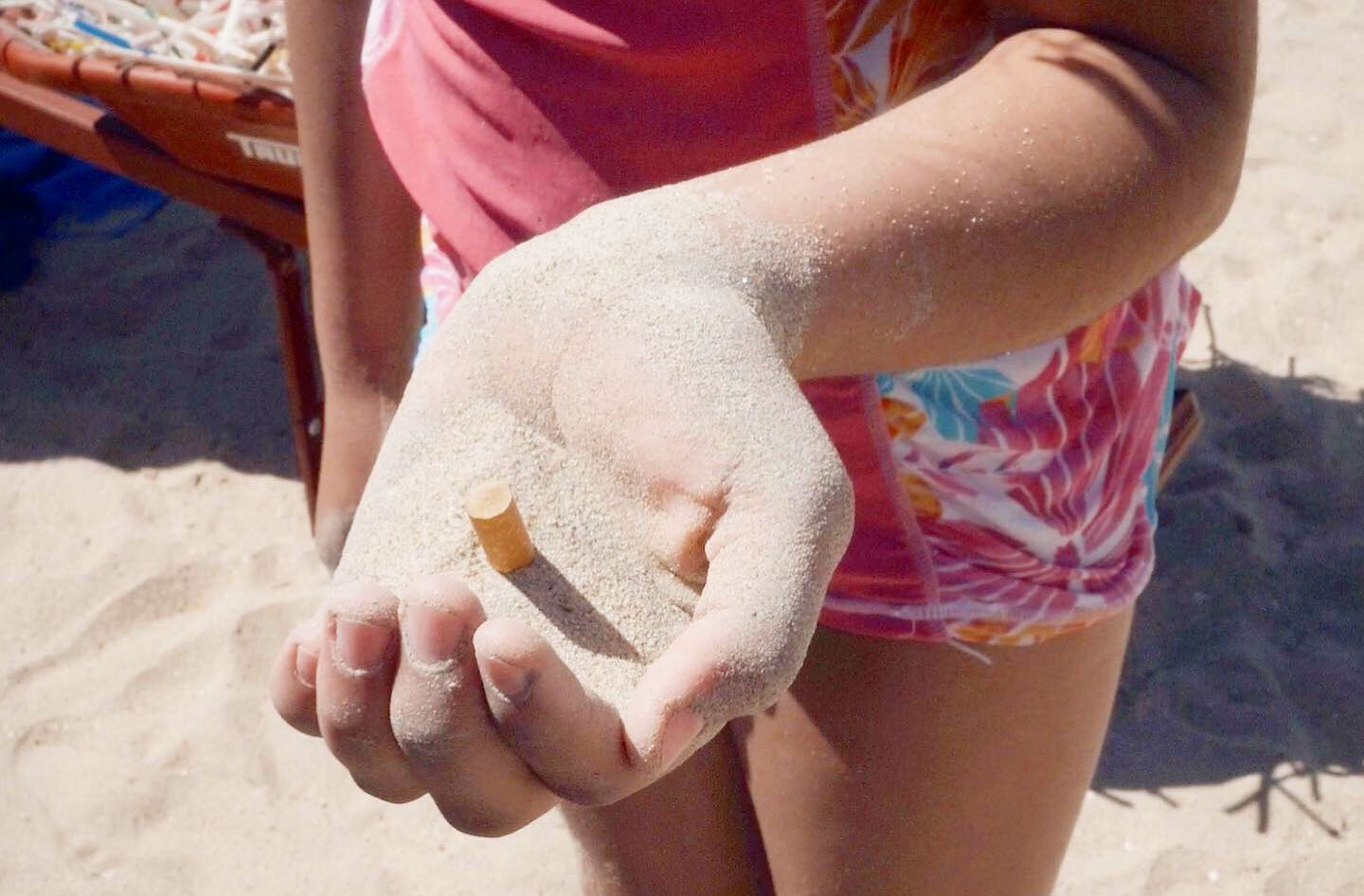 Open hand holds sand with a cigarette butt in it