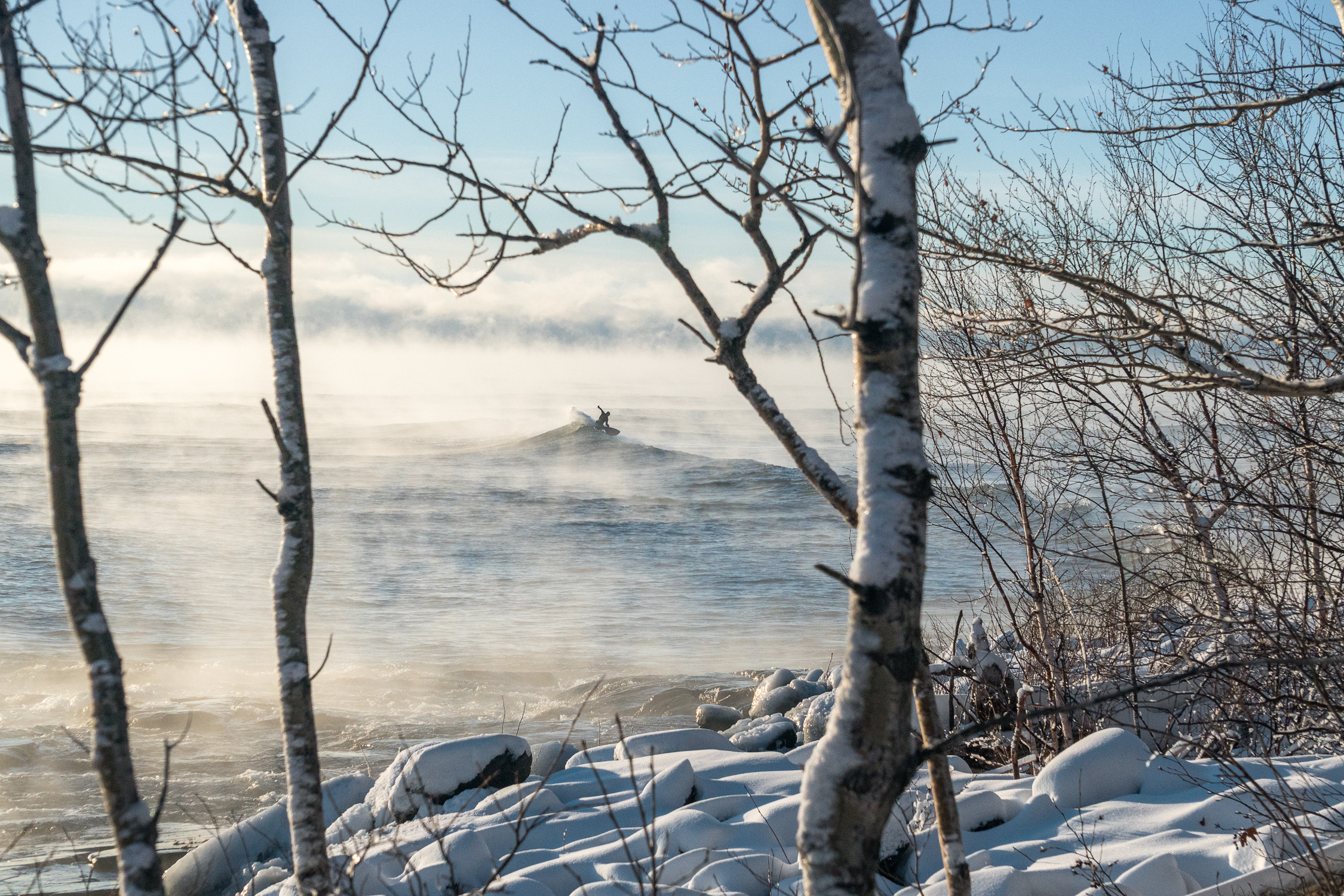 Snow covered shoreline looks out toward fog-covered water