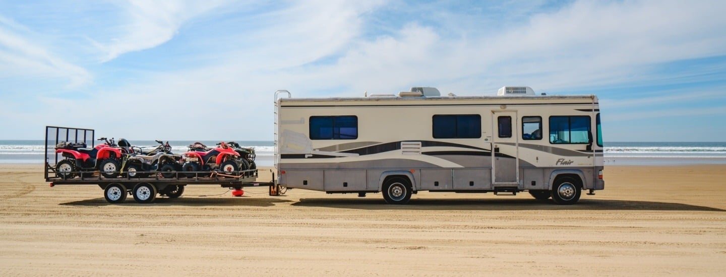 RV hauling Off-highway Vehicles Driving on the Beach at Oceano Dunes State Park, covered in tire tracks.