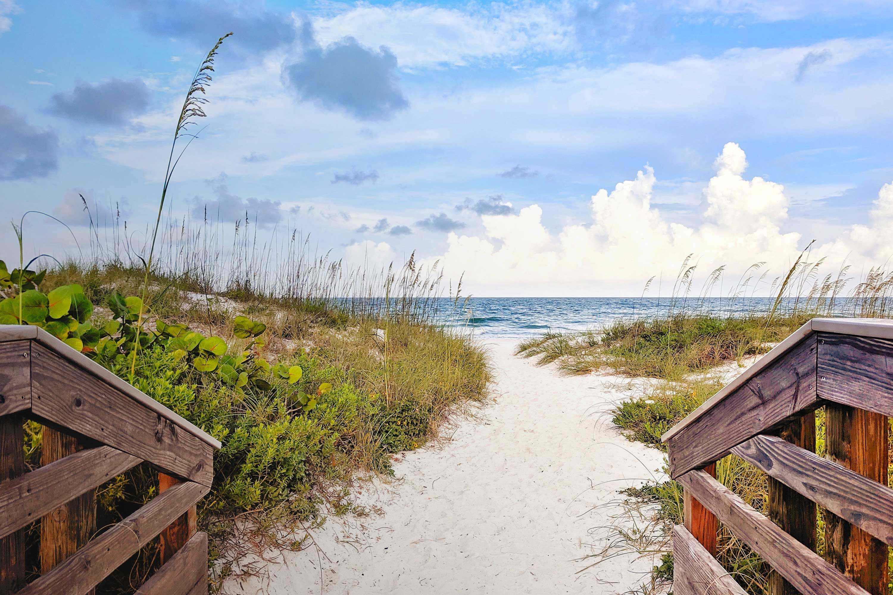 Sandy walkway leads to Florida beach with clouds in the background