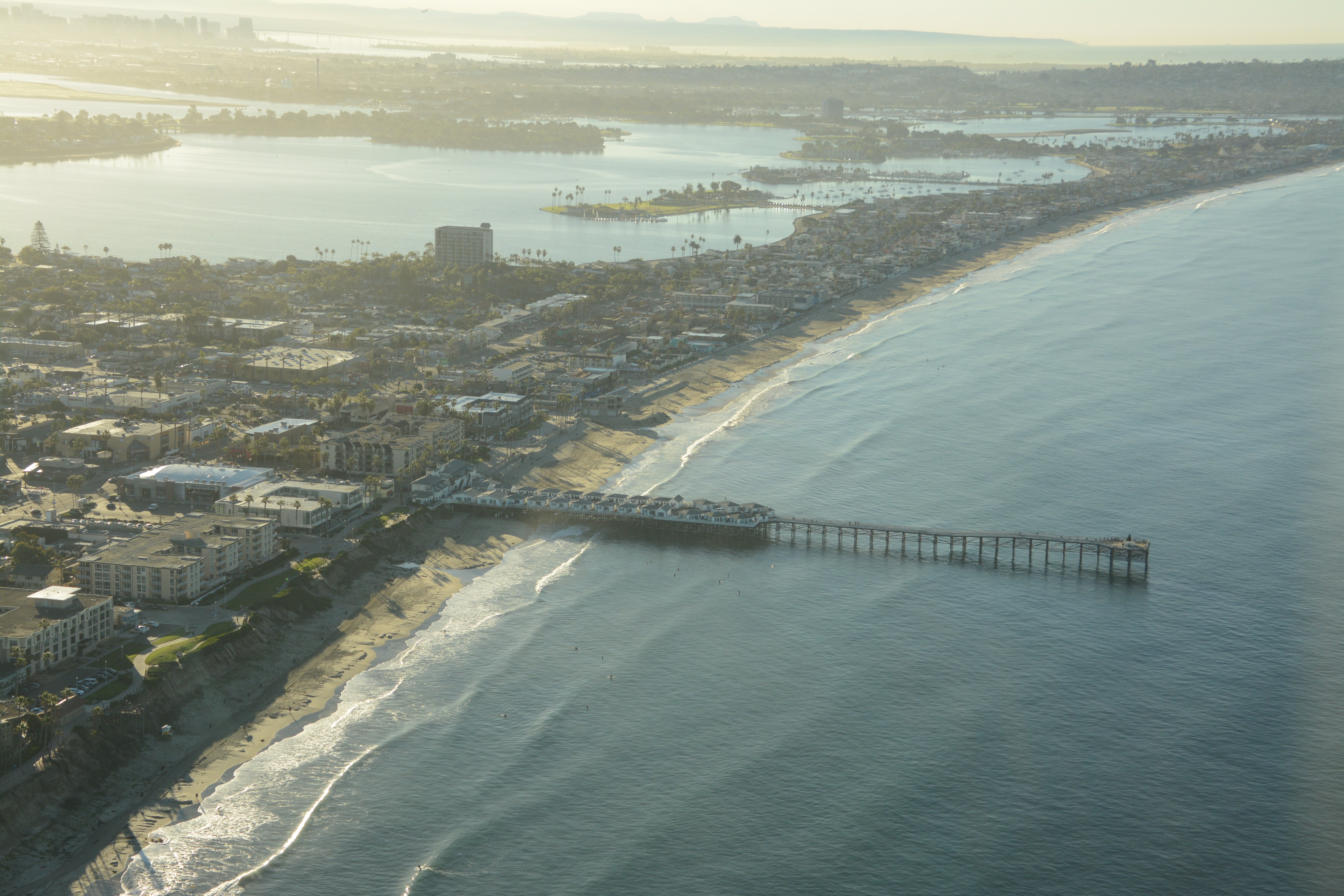 aerial photo of crystal pier in soft morning light. small swell lines the coast with soft rows of incoming waves.