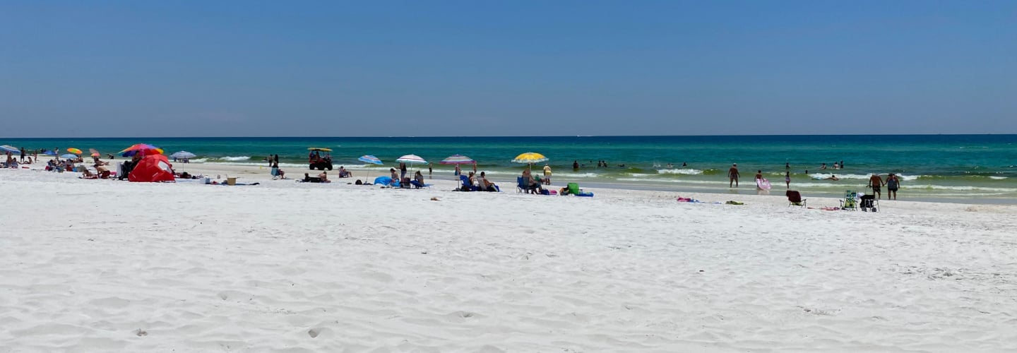 Walton County, Florida sandy shoreline with people lounging on the sand by the ocean with umbrellas and chairs
