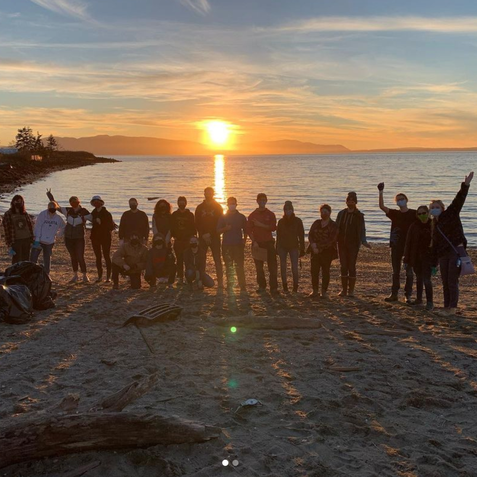 A sunset silhouette for a gropu of students standing shoulder to shoulder after a beach cleanup 