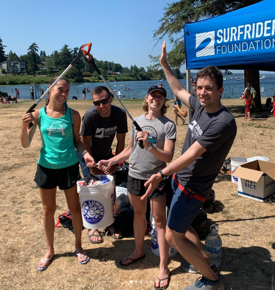 Four volunteers hold up their trash and pickers at a 2021 cleanup at Seward Park in Seattle