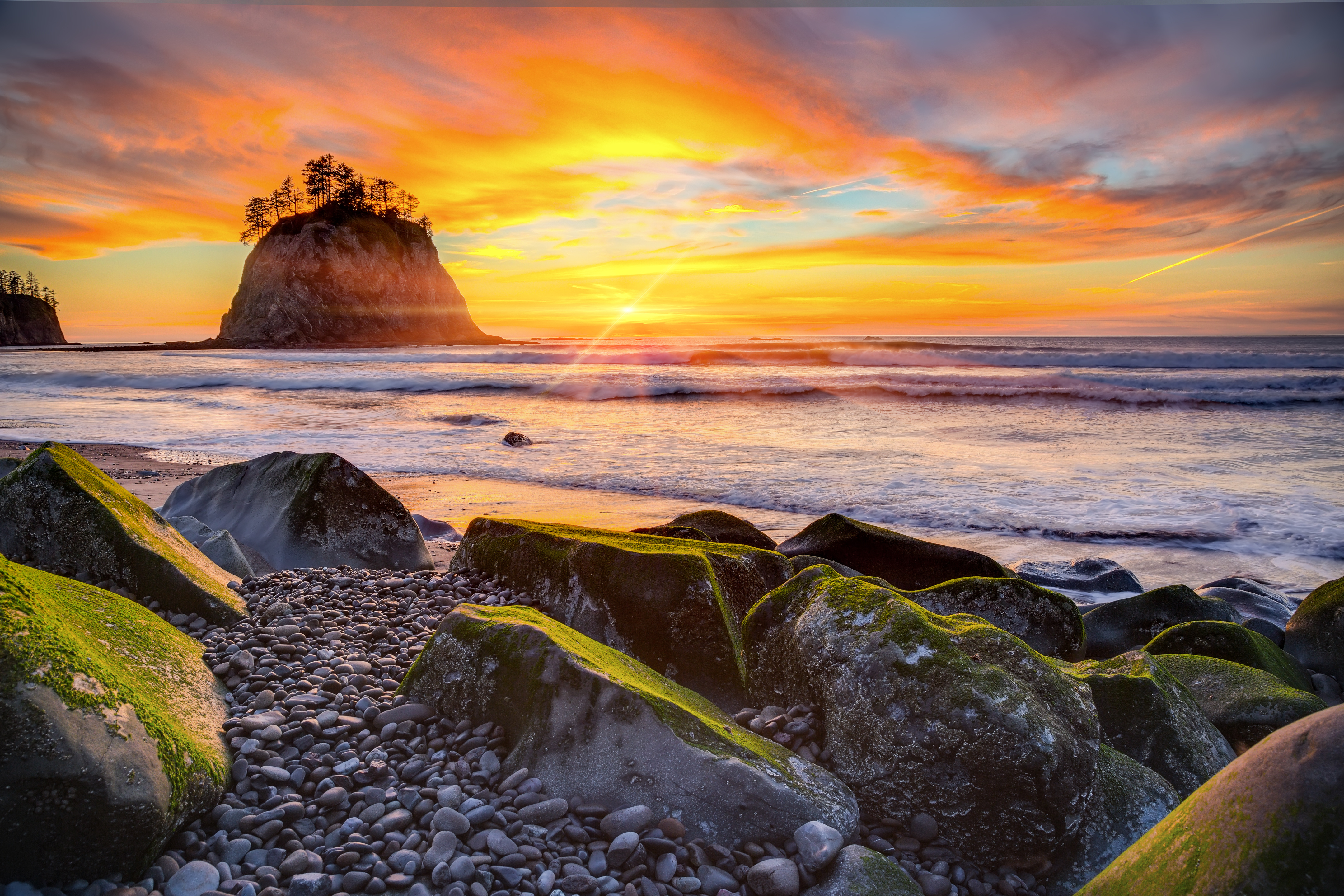 A brightly colored sunset view of a rocky beach with the silhouette of a haystack rock in the distance