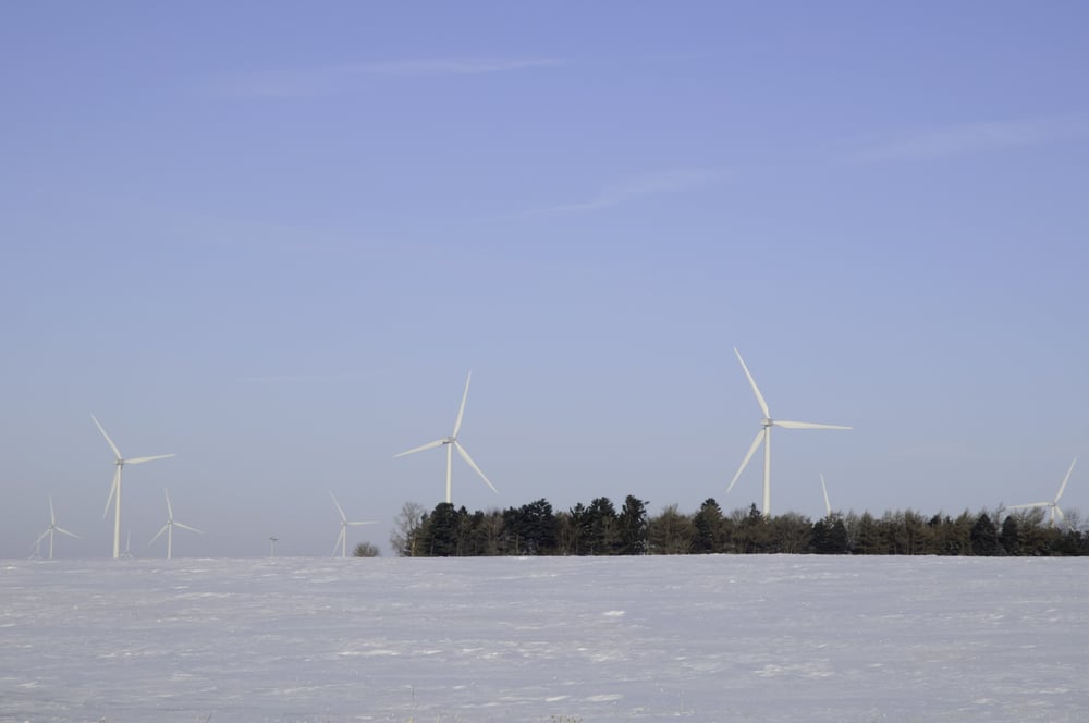Wind turbines above trees and snowy field on wintry morning in rural Illinois