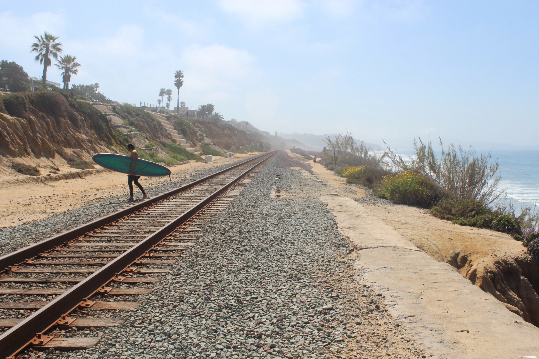 A surfer illegally crosses the train tracks to access the beach via a path down the bluff