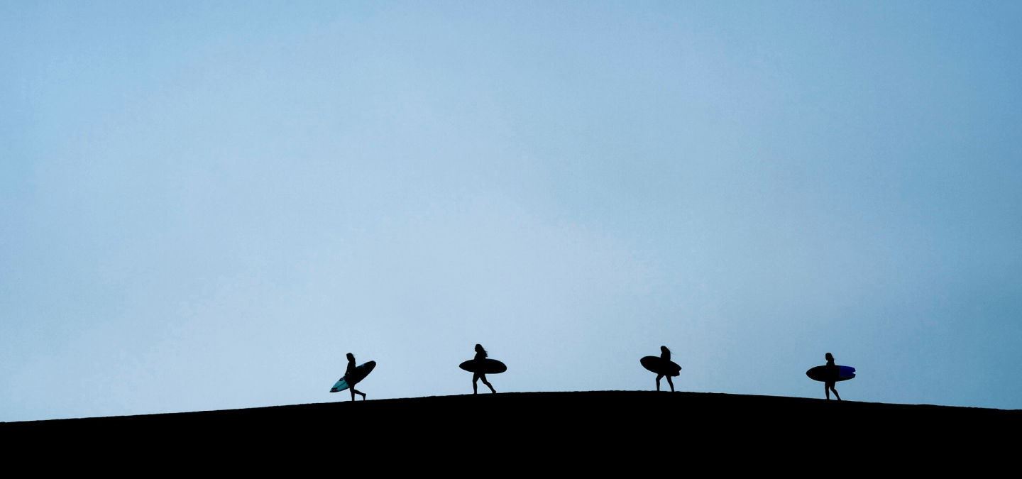 four surfers walking along hill